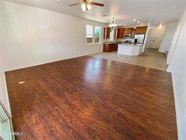 unfurnished living room with ceiling fan with notable chandelier and light hardwood / wood-style flooring