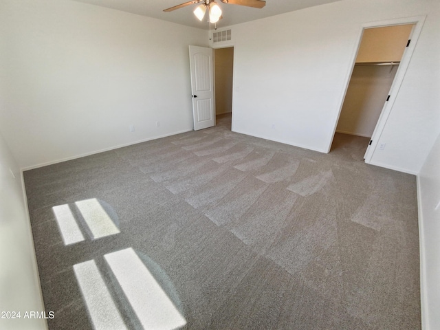 unfurnished bedroom with a walk in closet, carpet, and ceiling fan