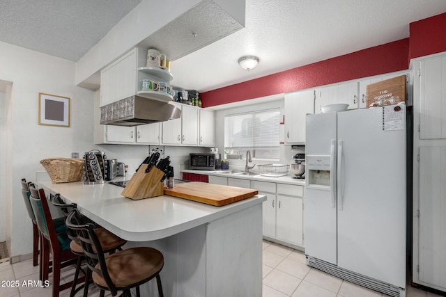 kitchen with kitchen peninsula, white cabinets, white fridge with ice dispenser, and sink