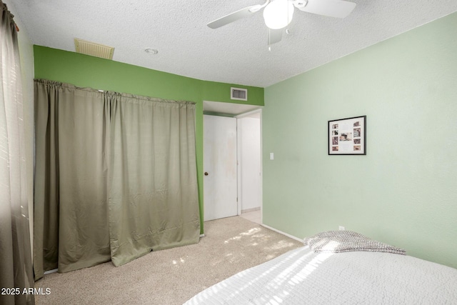 bedroom with ceiling fan, light colored carpet, and a textured ceiling