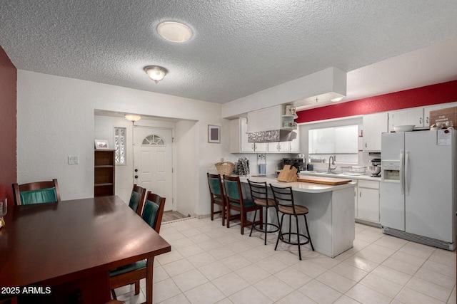 kitchen with white cabinets, a breakfast bar, white fridge with ice dispenser, and kitchen peninsula