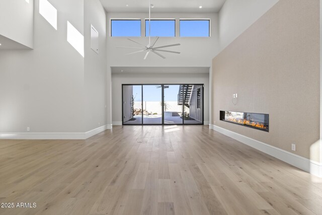 8503 S 9th Dr Unit 17, Phoenix, AZ 85041 - unfurnished living room featuring a towering ceiling, a ceiling fan, a glass covered fireplace, baseboards, and light wood finished floors