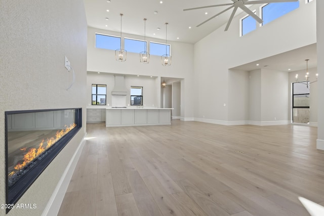 8503 S 9th Dr Unit 17, Phoenix, AZ 85041 - unfurnished living room featuring a high ceiling, a glass covered fireplace, ceiling fan, light wood-style flooring, and plenty of natural light
