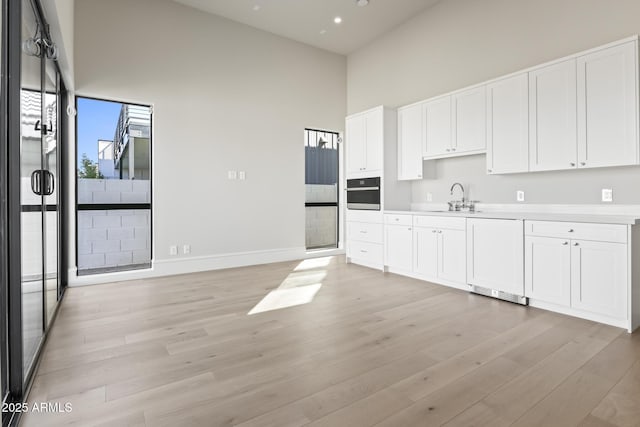 8503 S 9th Dr Unit 17, Phoenix, AZ 85041 - kitchen featuring stainless steel oven, light wood-style flooring, baseboards, white cabinetry, and a high ceiling