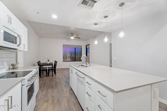 kitchen featuring white cabinets, hanging light fixtures, white appliances, sink, and an island with sink