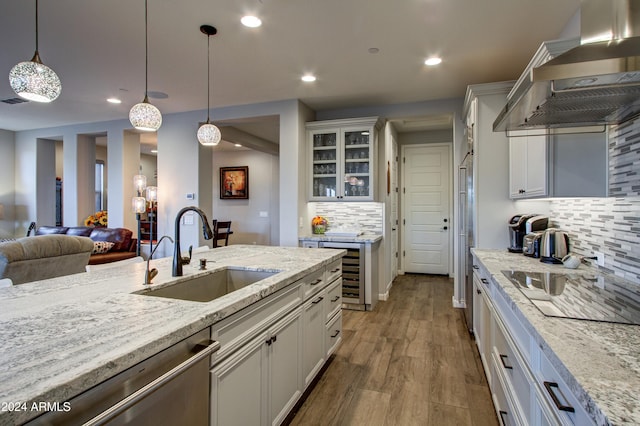 kitchen with pendant lighting, wall chimney exhaust hood, sink, backsplash, and white cabinetry