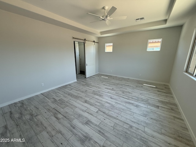 17324 W Royal Palm Rd, Waddell, AZ 85355 - empty room featuring a raised ceiling, a ceiling fan, a barn door, light wood-type flooring, and baseboards