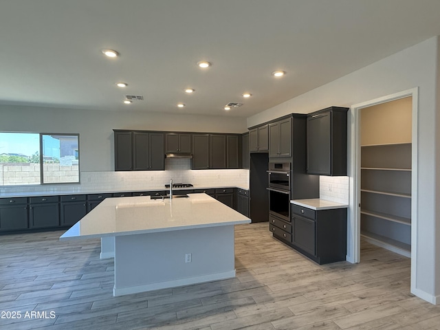 17324 W Royal Palm Rd, Waddell, AZ 85355 - kitchen featuring decorative backsplash, light wood-style flooring, a kitchen island with sink, light countertops, and recessed lighting