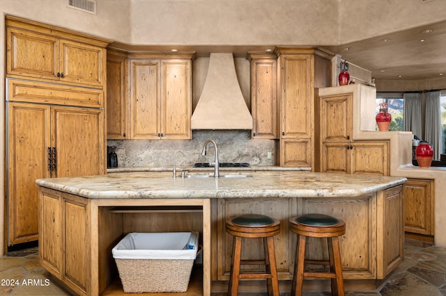 kitchen featuring paneled built in refrigerator, light stone counters, a kitchen island with sink, and custom exhaust hood