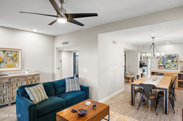 living room with ceiling fan with notable chandelier and light hardwood / wood-style floors