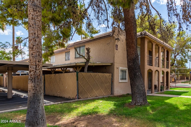 view of side of home with a balcony, a lawn, and a carport