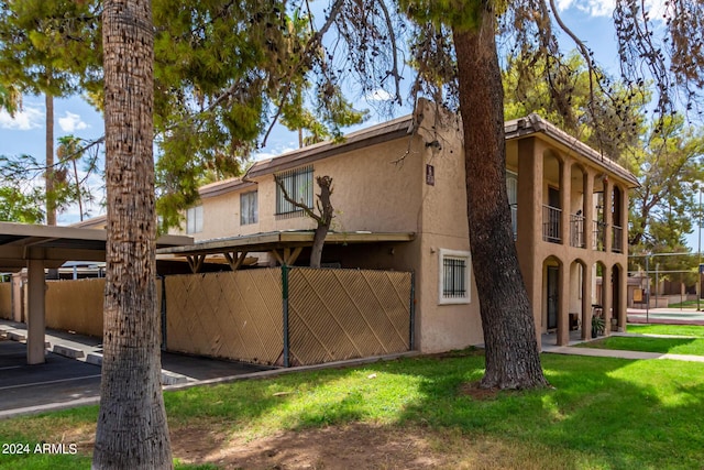 exterior space featuring a balcony, stucco siding, a yard, and fence