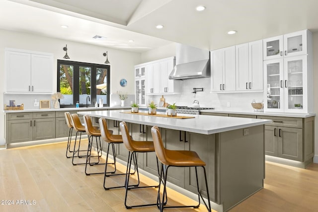 kitchen featuring a large island, wall chimney exhaust hood, white cabinetry, and light wood-type flooring