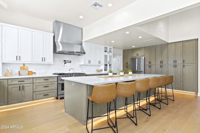 kitchen with wall chimney exhaust hood, light hardwood / wood-style floors, a spacious island, a breakfast bar area, and appliances with stainless steel finishes