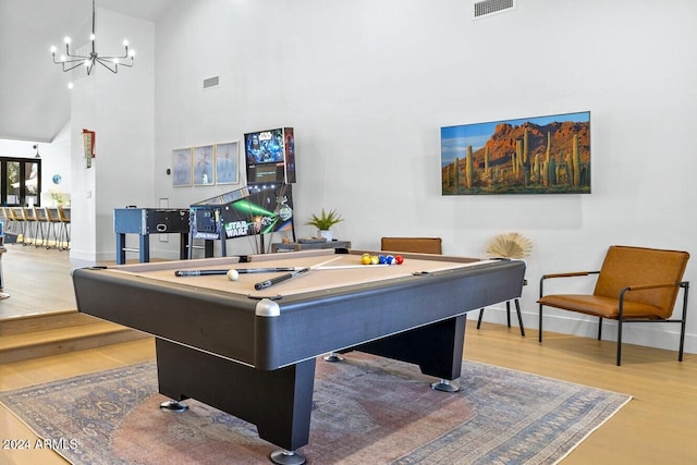 playroom featuring billiards, an inviting chandelier, a towering ceiling, and light wood-type flooring