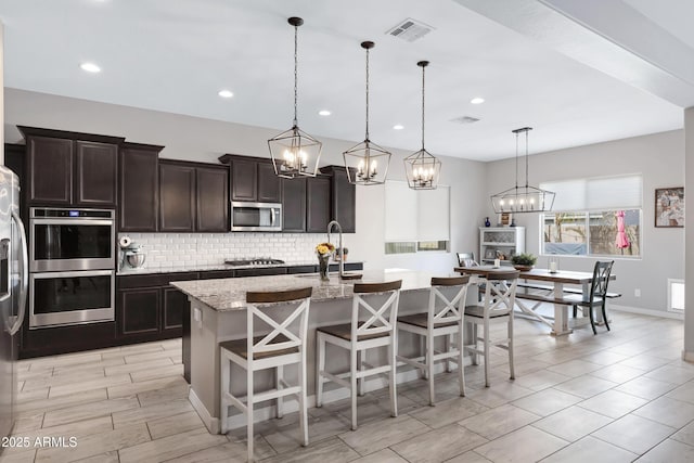 kitchen featuring hanging light fixtures, an island with sink, stainless steel appliances, and a kitchen breakfast bar