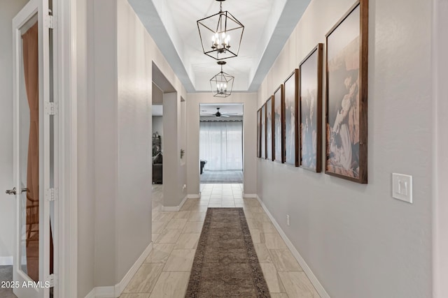 hall featuring a tray ceiling and a chandelier