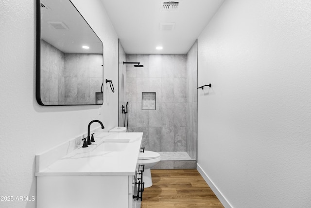 bathroom featuring tiled shower, wood-type flooring, vanity, and toilet