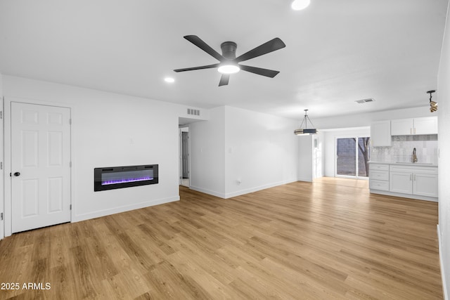 unfurnished living room with heating unit, ceiling fan, and light hardwood / wood-style flooring