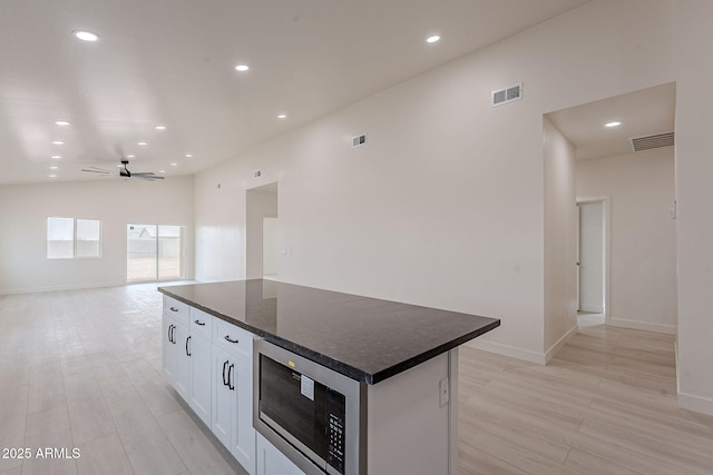 kitchen featuring ceiling fan, white cabinetry, a kitchen island, built in microwave, and light wood-type flooring