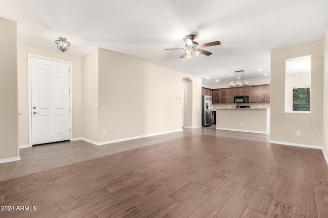 unfurnished living room featuring ceiling fan with notable chandelier and light wood-type flooring