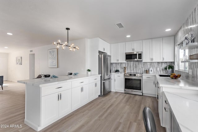 kitchen with white cabinetry, hanging light fixtures, light hardwood / wood-style floors, and appliances with stainless steel finishes