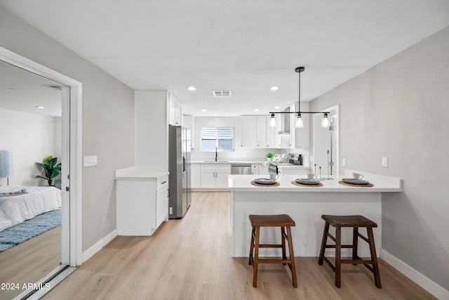 kitchen featuring white cabinets, hanging light fixtures, light hardwood / wood-style flooring, kitchen peninsula, and stainless steel appliances