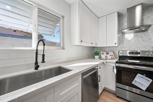 kitchen with appliances with stainless steel finishes, sink, white cabinetry, and wall chimney range hood