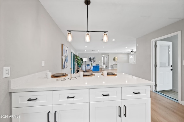 interior space with kitchen peninsula, light wood-type flooring, ceiling fan, pendant lighting, and white cabinetry