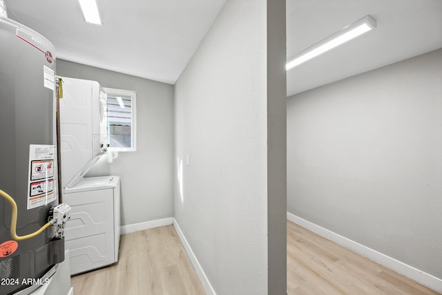 laundry room featuring water heater, stacked washer and dryer, and light wood-type flooring