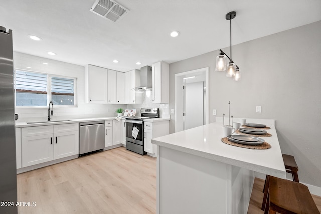 kitchen featuring pendant lighting, white cabinets, wall chimney range hood, sink, and appliances with stainless steel finishes