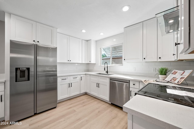 kitchen featuring backsplash, white cabinets, sink, light wood-type flooring, and stainless steel appliances