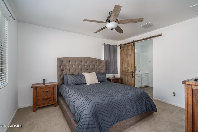 bedroom featuring ceiling fan, light colored carpet, connected bathroom, and a barn door