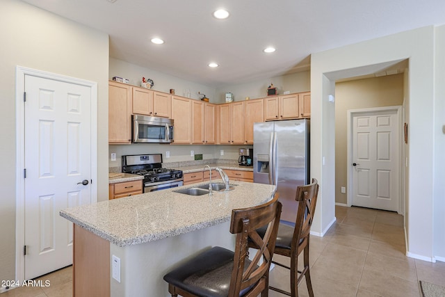 kitchen with appliances with stainless steel finishes, a kitchen breakfast bar, light brown cabinetry, sink, and an island with sink