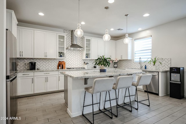 kitchen with wall chimney range hood, a kitchen island, a kitchen bar, white cabinetry, and stainless steel appliances