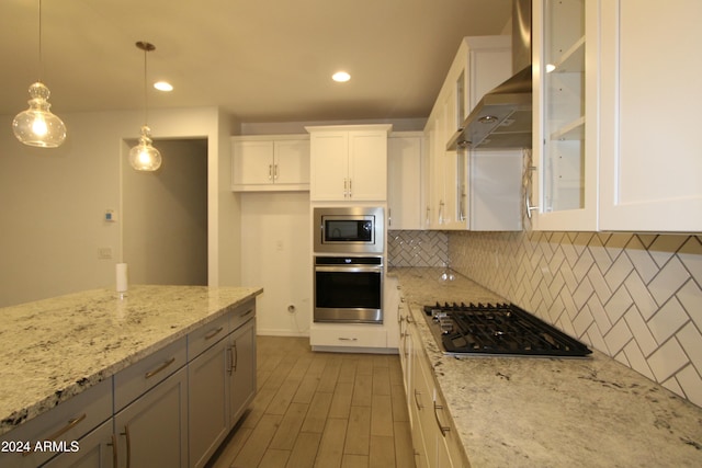 kitchen featuring light stone countertops, wall chimney exhaust hood, hanging light fixtures, white cabinets, and appliances with stainless steel finishes