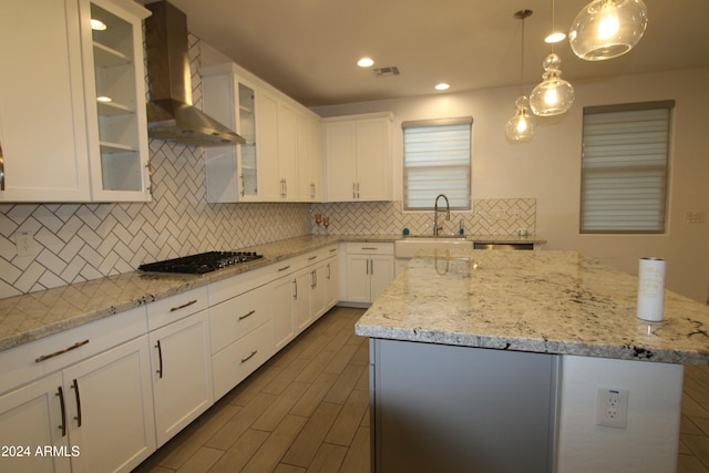 kitchen with stainless steel gas stovetop, a center island, wall chimney range hood, and white cabinetry