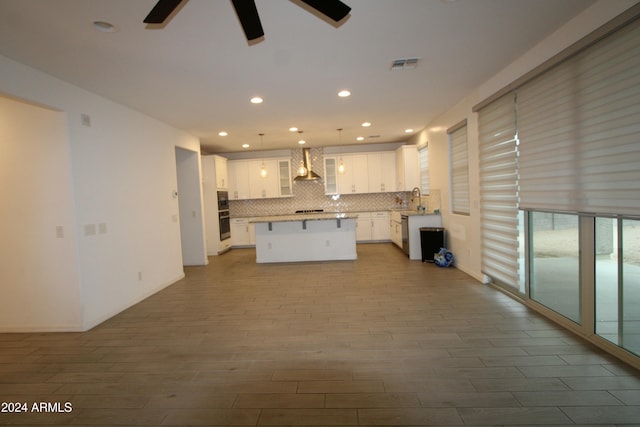 kitchen featuring wall chimney range hood, a kitchen island, backsplash, pendant lighting, and white cabinets