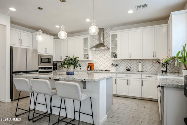 kitchen with white cabinets, a center island, stainless steel appliances, and wall chimney range hood