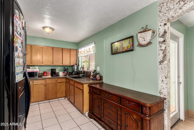 kitchen featuring black refrigerator with ice dispenser, a sink, dark countertops, stainless steel microwave, and brown cabinets