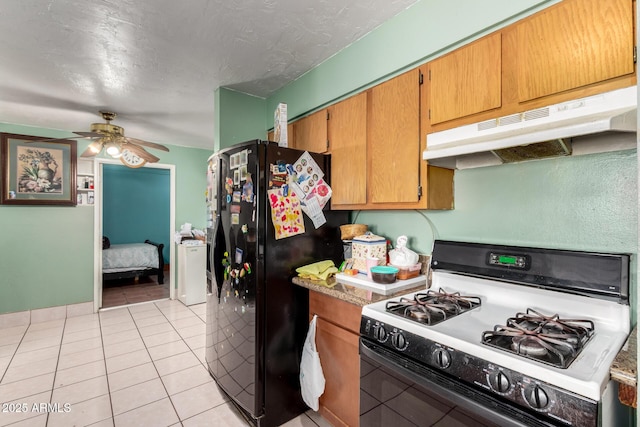 kitchen featuring gas stove, under cabinet range hood, freestanding refrigerator, light tile patterned flooring, and a ceiling fan