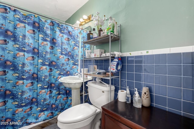 bathroom featuring toilet, a shower with shower curtain, tile walls, and a wainscoted wall