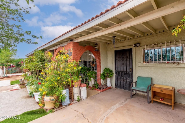 property entrance featuring a tiled roof, stucco siding, and fence