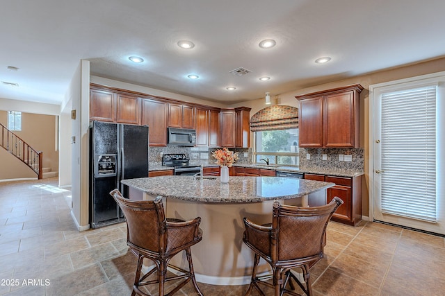 kitchen featuring light stone counters, backsplash, a kitchen bar, a center island with sink, and black appliances