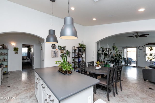 kitchen with arched walkways, pendant lighting, dark countertops, open floor plan, and white cabinets