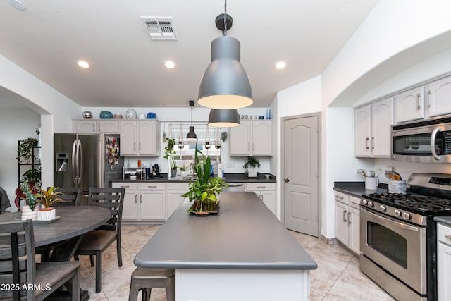 kitchen with stainless steel appliances, visible vents, white cabinets, a center island, and decorative light fixtures