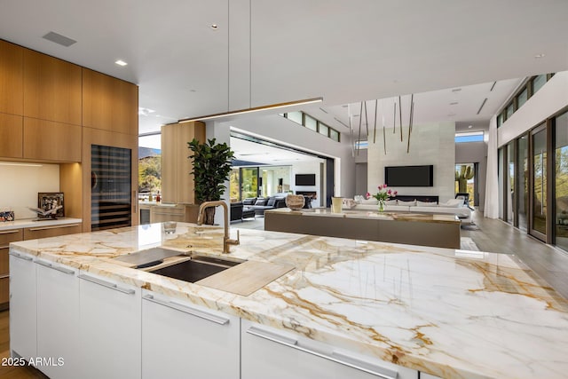 kitchen featuring decorative light fixtures, sink, white cabinets, a high ceiling, and light stone countertops