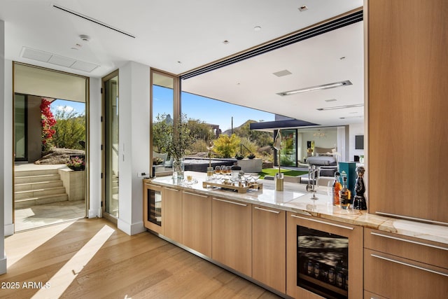 bar with beverage cooler, light stone countertops, and light wood-type flooring