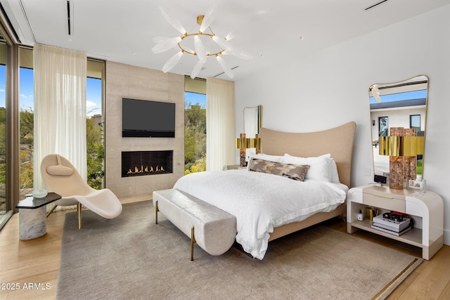 bedroom with a fireplace, a wall of windows, and light wood-type flooring