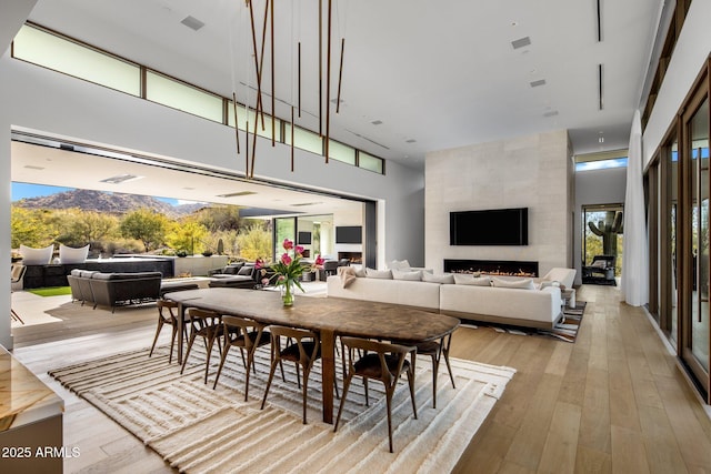 dining space with a tile fireplace, a towering ceiling, a wealth of natural light, and light wood-type flooring